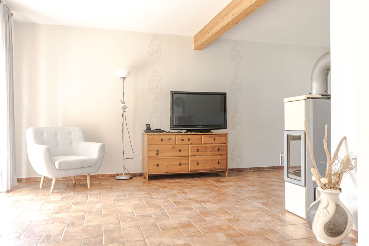 Wohnraum mit Sessel, Kaminofen und Flachbildfernseher auf einer Holzkommode