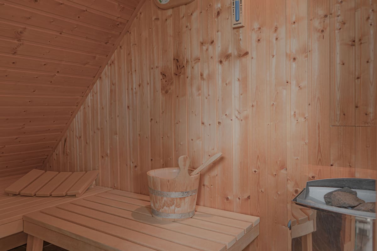 Sauna aus hellem Holz mit Sitzbänken, Kübel und Saunaofen
